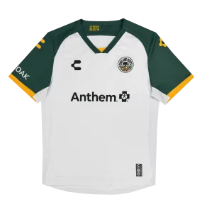 The Unisex Oakland Roots SC 2025 Second Kit features a white and dark green jersey inspired by Oakland sports history. It has dark green short sleeves with yellow trim and logos, a circular emblem, "Charly" logo, "Anthem" with a cross s